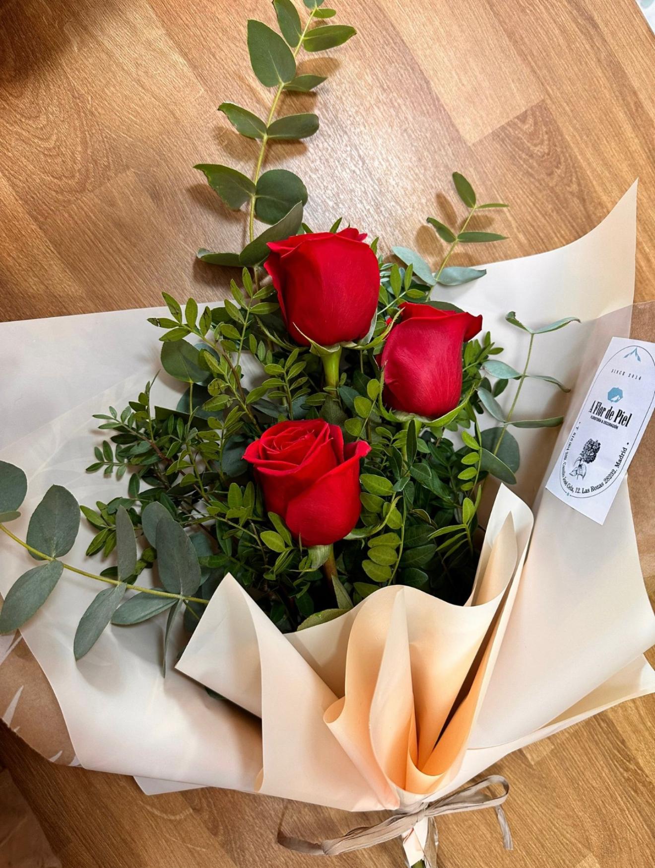 Ramo de tres rosas rojas con verdes, envuelto en papel claro